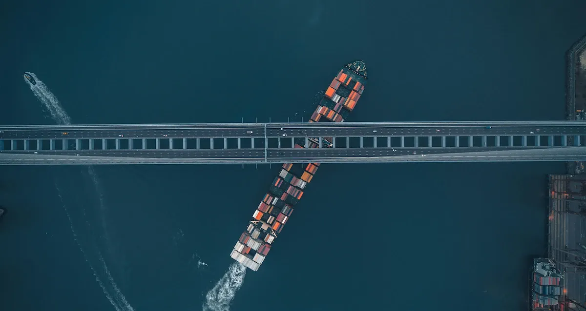 Aerial view of container ship passing under bridge showing port constraints and clearance limits